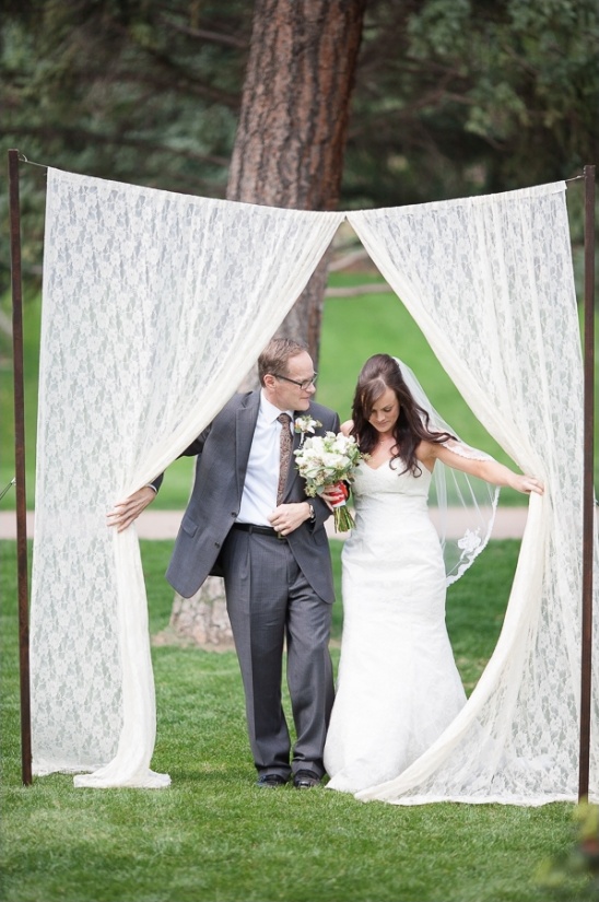 Bride and groom stand under lace wedding arch