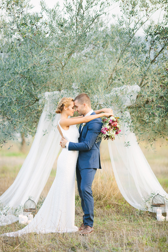 Couple embraces at wedding ceremony under draped tree