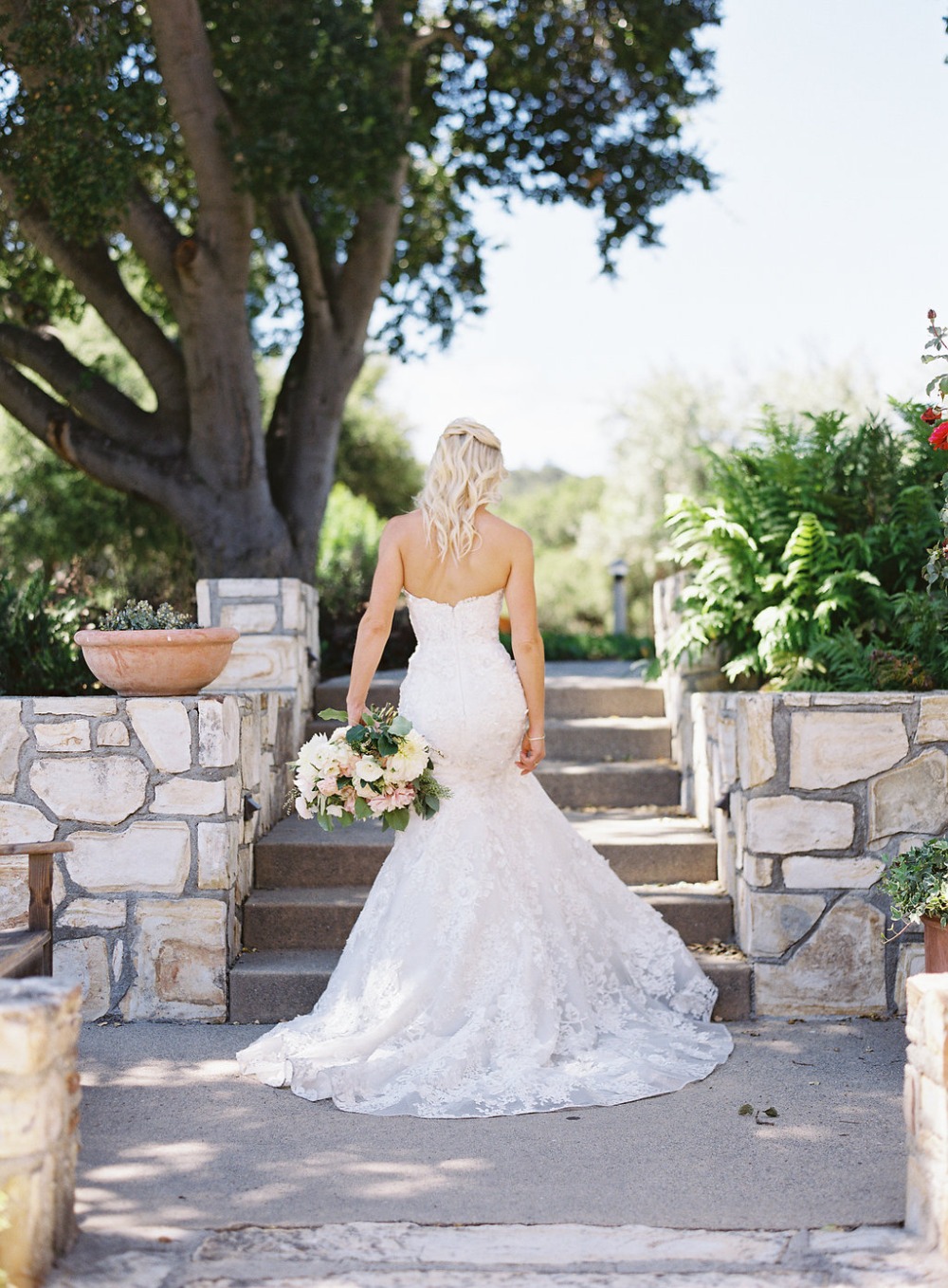 Bride in lace gown holds bouquet walking to wedding
