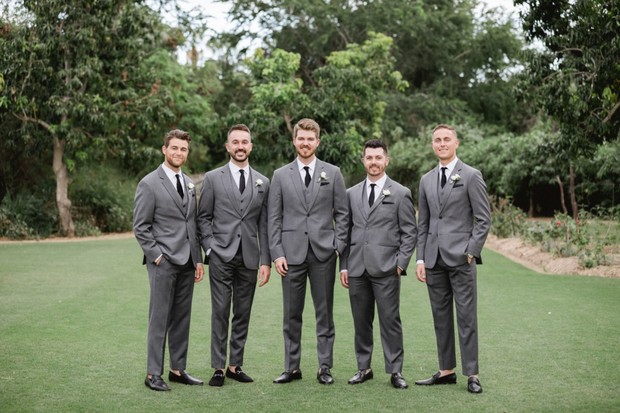 Here are a few options for the alt tag:

**Option 1 (Focus on attire):**
Groomsmen in grey suits at outdoor wedding portrait

**Option 2 (Focus on occasion):**
Wedding groomsmen in grey suits outdoor group photo

**Option 3 (More descriptive):**
Outdoor wedding groomsmen in grey suits formal pose

**Option 4 (Slightly more expressive):**
Dapper groomsmen in grey suits outdoor wedding pose

Considering the image and SEO best practices, **Option 4 Dapper groomsmen in grey suits outdoor wedding pose** is the most expressive and SEO-friendly within the character limits 

**Final Answer:** Dapper groomsmen in grey suits outdoor wedding pose
