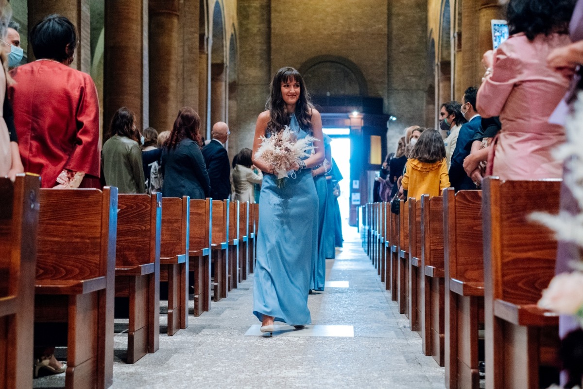 Bridesmaid in blue walks down aisle in church wedding