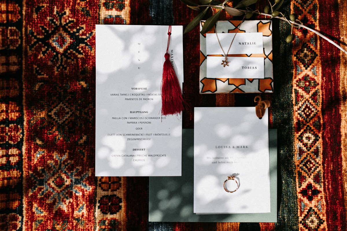 Wedding menu cards, place cards, and rings on a rug