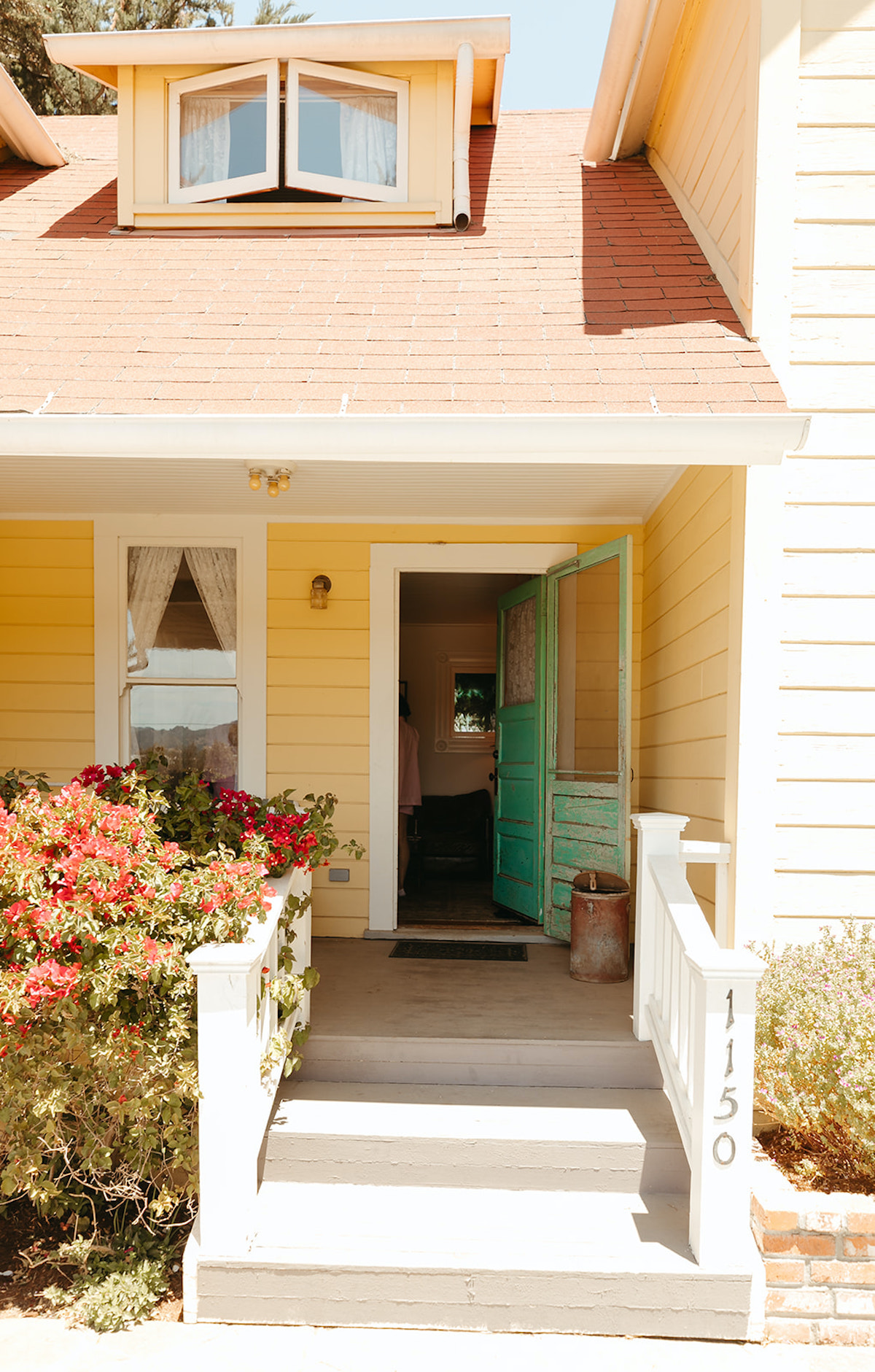 Charming yellow house entrance with red roof and flowers
