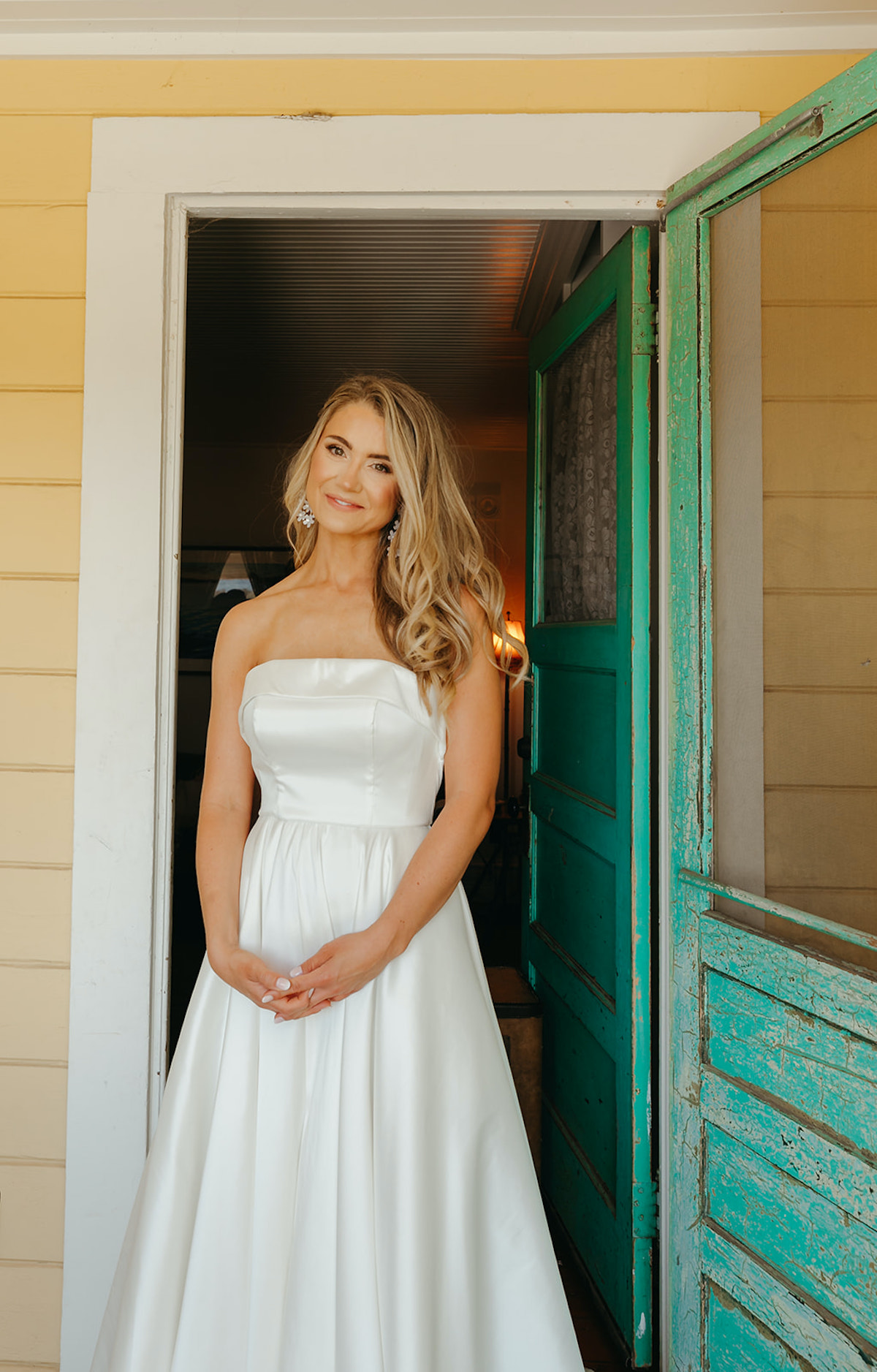 Bride in strapless white gown smiles in sunny doorway